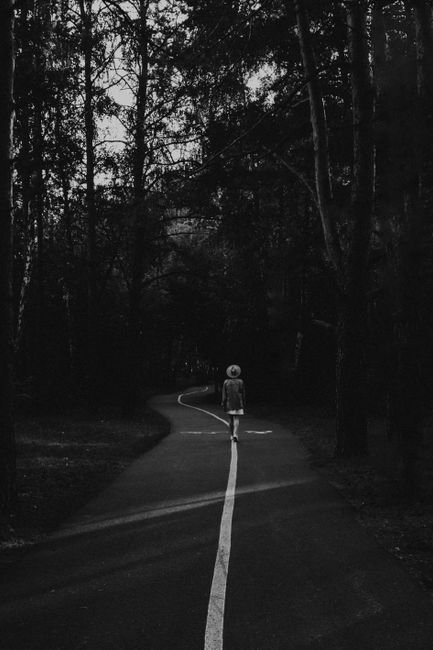 A lone woman walking down a forest path in black and white, conveying solitude.