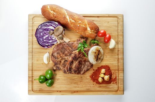 Top view of steak, bread, and vegetables arranged on a wooden chopping board.