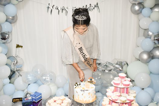 A woman at a birthday party cutting a cake surrounded by pastel balloons and cupcakes.