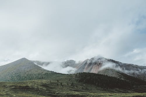 Green Grass Field Near Mountains Under White Clouds