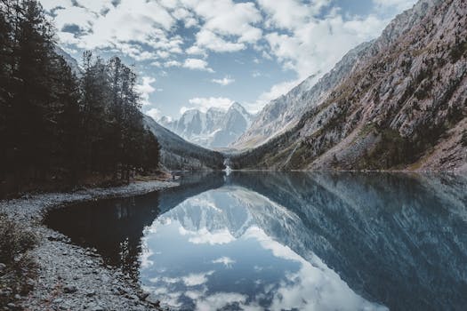 A tranquil mountain lake reflecting rugged peaks and a clear sky, creating a picturesque wilderness scene.