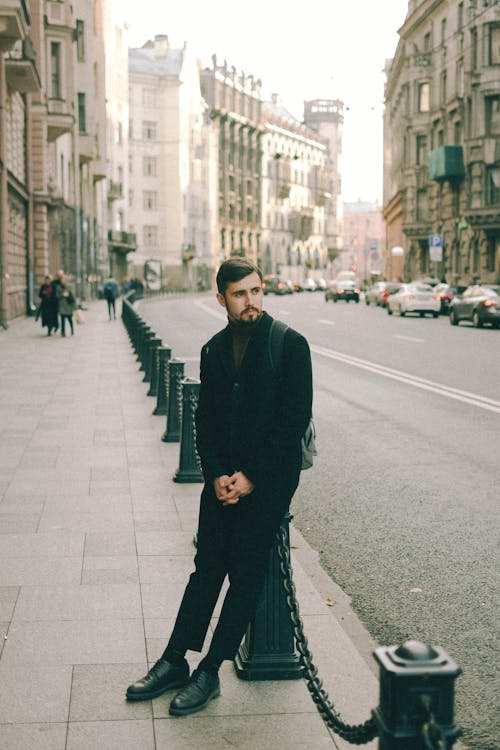 Free Young bearded man wearing black outfit standing in street of old town Stock Photo