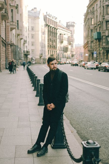 Man in black coat on city sidewalk with townhouse backdrop.
