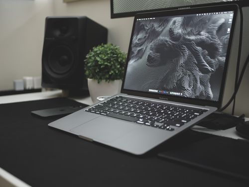 Free A sleek workspace featuring a laptop, speaker, and plant, showcasing modern technology and design. Stock Photo