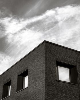 Low angle view of a modern brick building against a cloudy sky, showcasing architectural lines in monochrome.