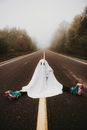 Person in ghost costume and roller skates sitting on foggy road