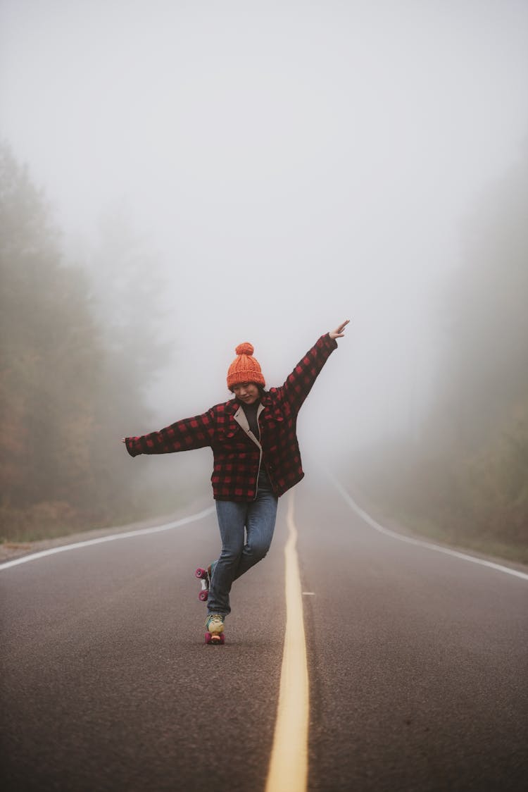 Woman In Orange Beanie Roller Skating On Empty Foggy Road