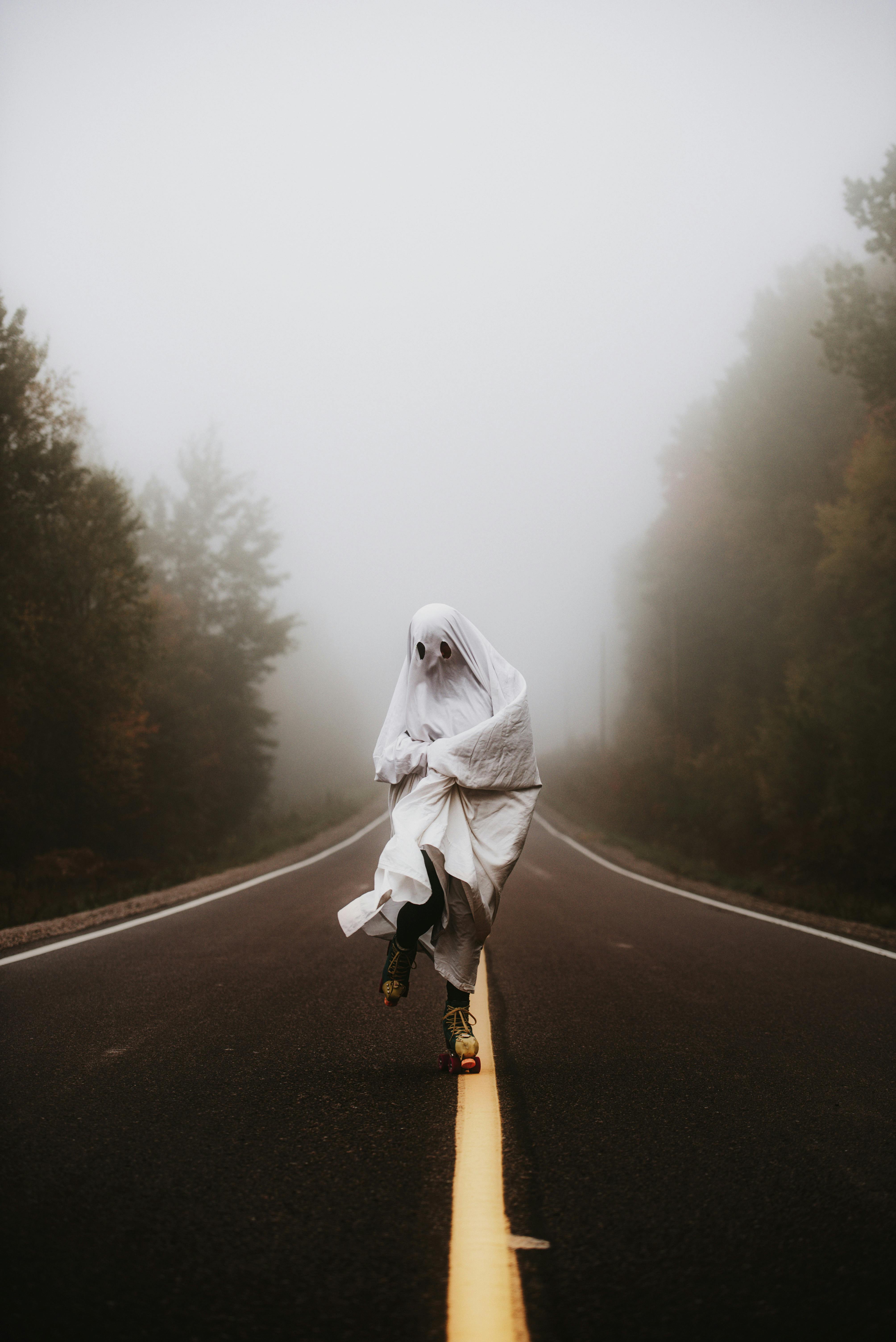 Foggy road with a person in a ghost costume roller skating. Eerie and playful atmosphere.