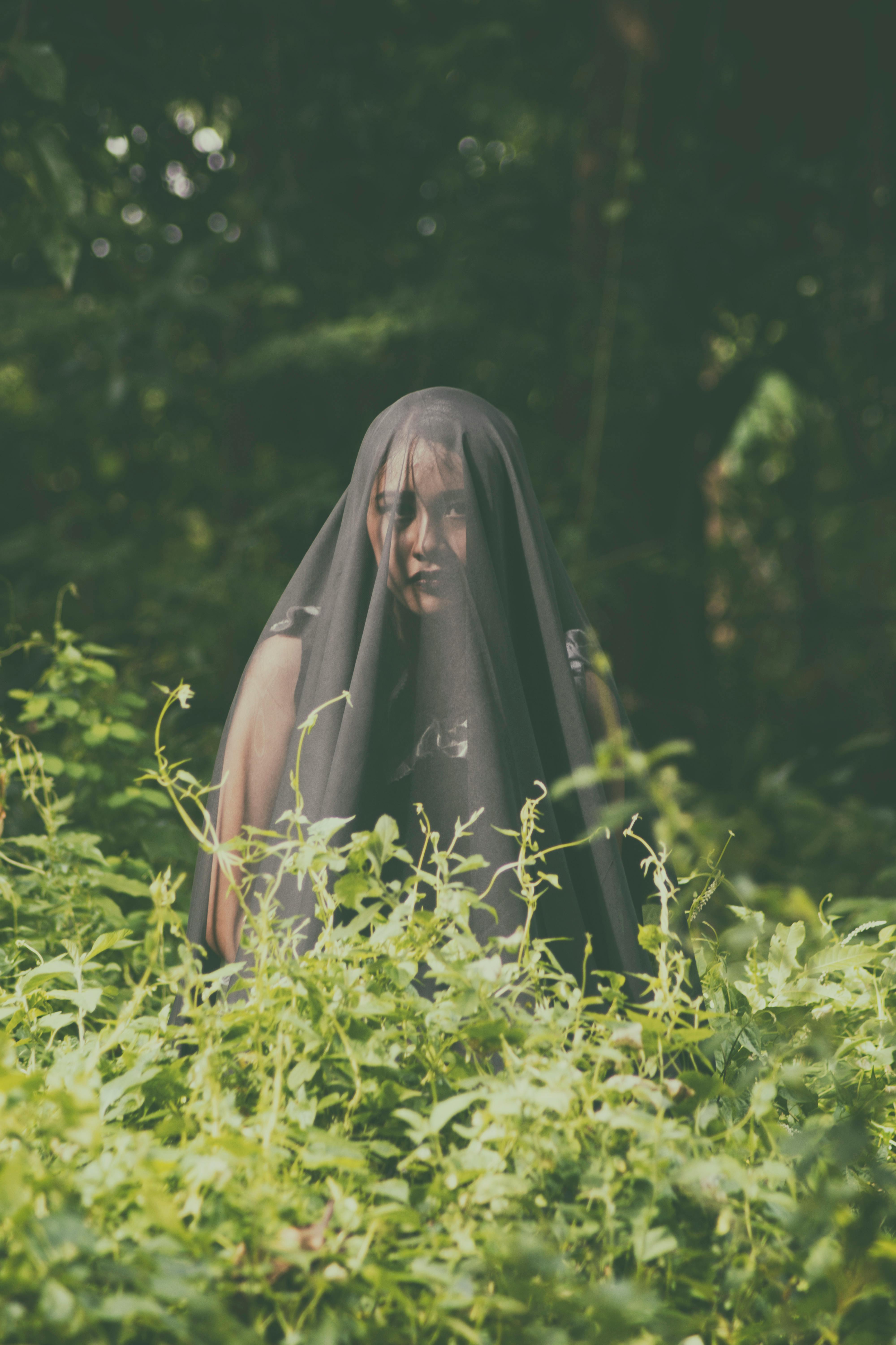 一位戴着深色面纱的女人融入森林环境，营造出神秘的氛围