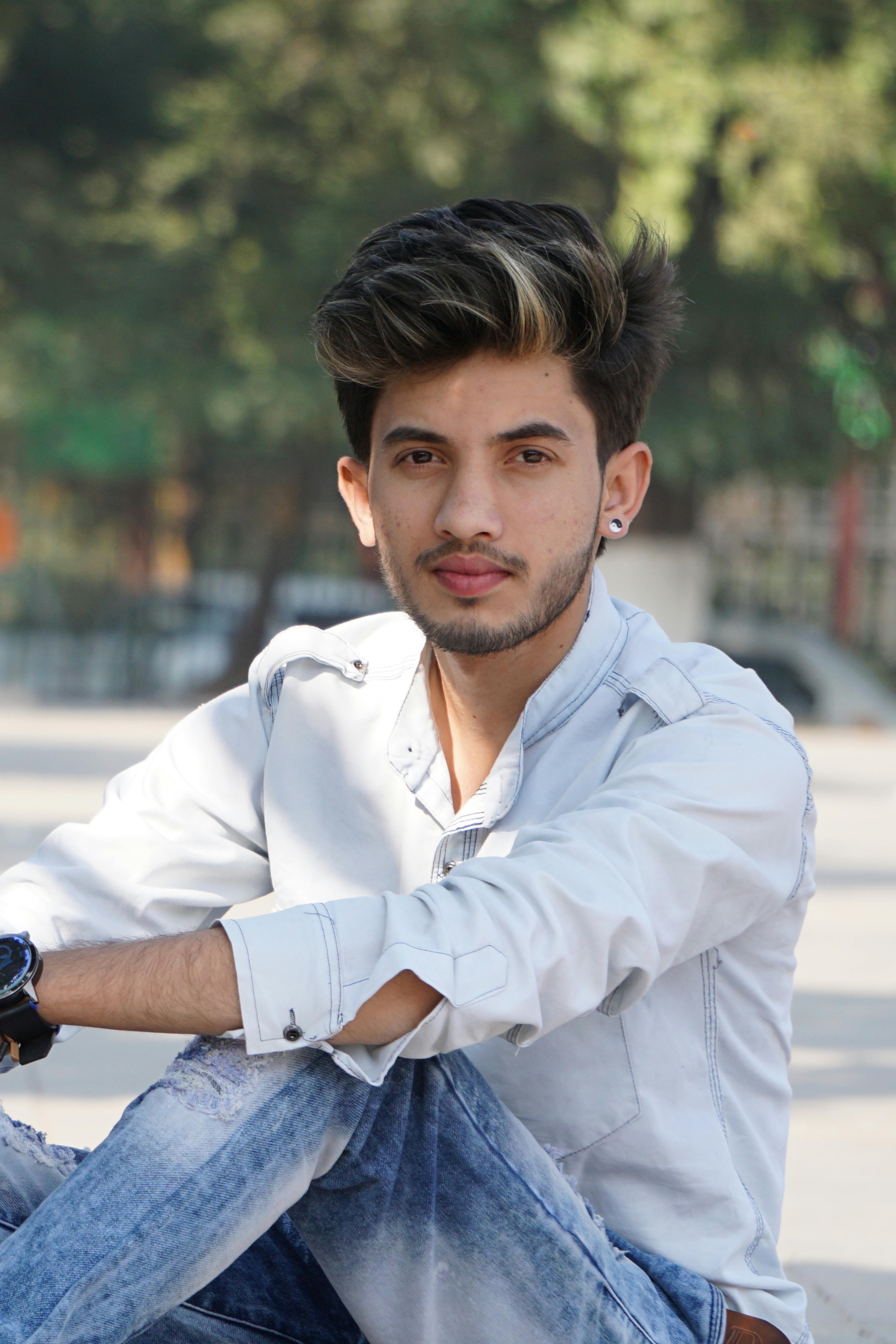 A fashionable young adult male posing outdoors with trees in background.