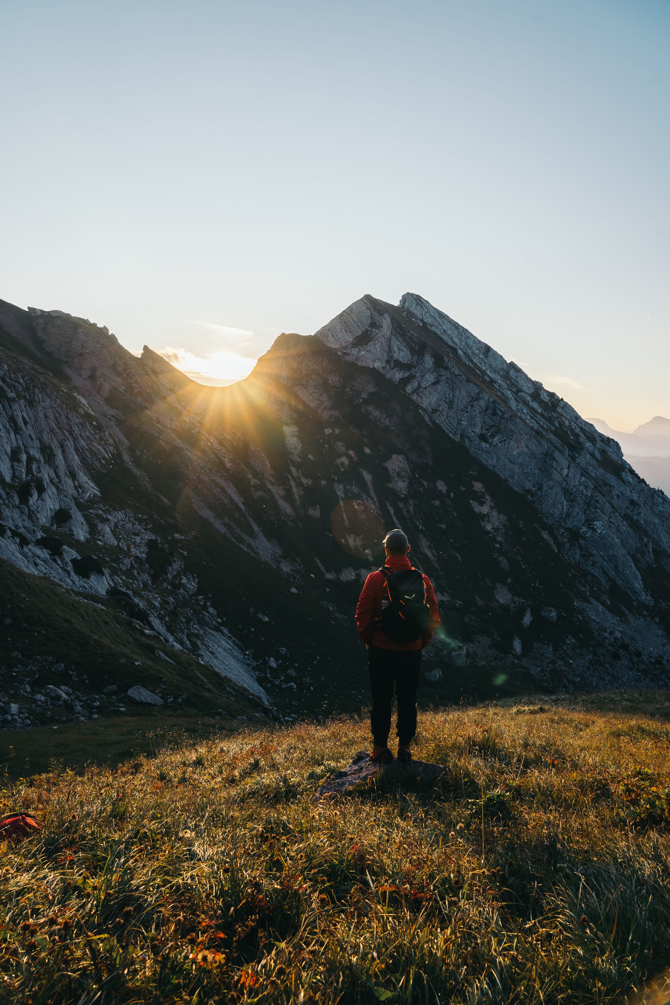 A hiker stands in awe watching the sunrise over a majestic mountain range.