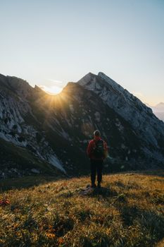 A hiker stands in awe watching the sunrise over a majestic mountain range.