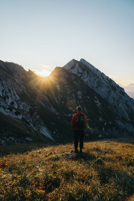 A hiker stands in awe watching the sunrise over a majestic mountain range.
