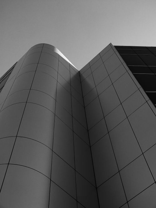 Free Low angle shot of a modern highrise building with curvy concrete facade in grayscale. Stock Photo