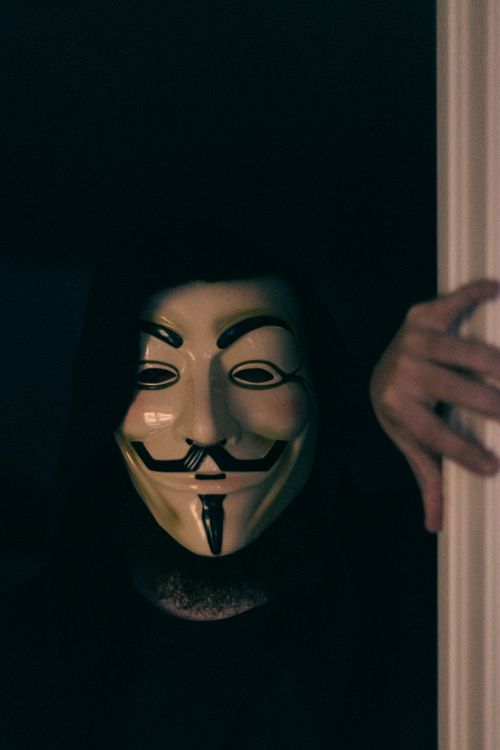 Free Person wearing a Guy Fawkes mask, symbolizing anonymity and mystery in a dark setting. Stock Photo