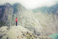 一名穿着红色夹克的人在大雾天气中，从岩石山上俯瞰宁静的高山湖泊，欣赏着令人惊叹的景色