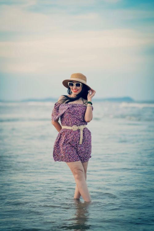 Free Woman in floral dress and hat smiling on sunny beach with blue skies. Stock Photo