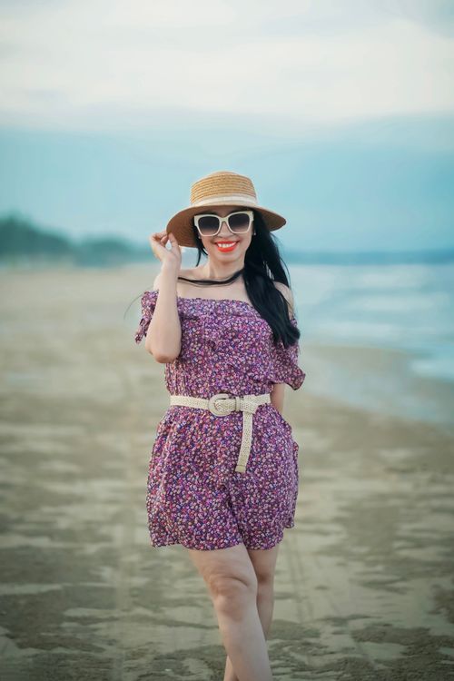 Free Elegant woman in a floral dress poses confidently on a sunny beach, capturing a stylish summer vibe. Stock Photo