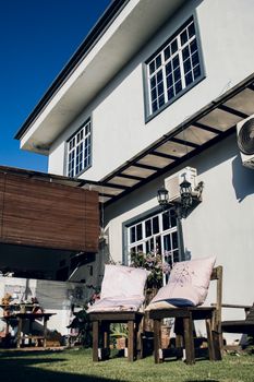 Charming outdoor setting featuring rustic chairs and pillows in a sunlit backyard with modern architecture.