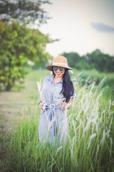 Smiling woman with long hair wears a sunhat in a grassy field under daylight.