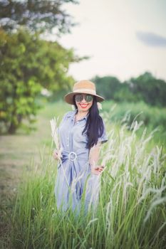 A joyful woman in a blue dress and sun hat stands amid green grass, smiling and enjoying a sunny day.