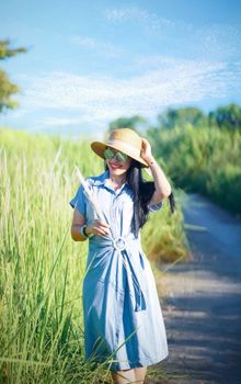 A woman in a blue dress and straw hat enjoying a sunny day in a grassy field.