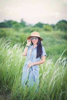 A woman in a blue dress and straw hat smiles happily in a lush green field, enjoying the summer day.