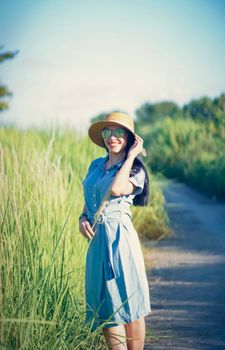 Stylish woman in a straw hat smiles amidst lush greenery on a sunny day.