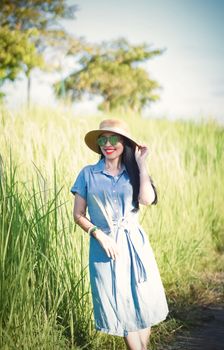 Woman in a blue dress and straw hat smiling in a sunny field, embodying summer joy.