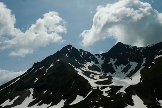 Stunning view of snow-capped mountains and cloud-filled blue sky in winter setting.