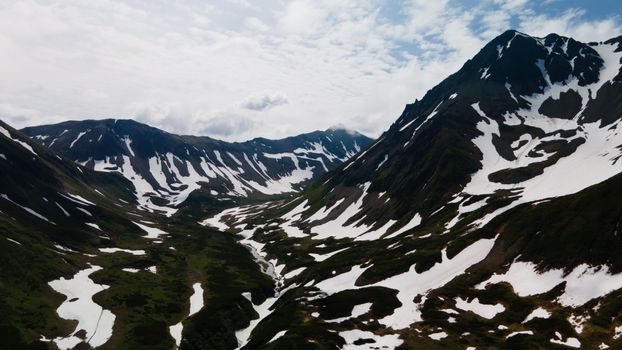 Stunning aerial view of the snow-dotted Kamchatka mountains during summer, showcasing nature's beauty.