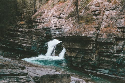 Free Beautiful waterfall flowing between rugged rock formations in a serene forest setting. Stock Photo