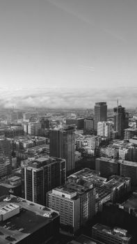 Dramatic black and white aerial view of a modern cityscape featuring tall skyscrapers and a cloudy sky.