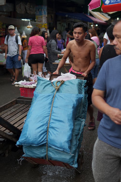 Photo of a Shirtless Man Pushing a Cart with Sacks