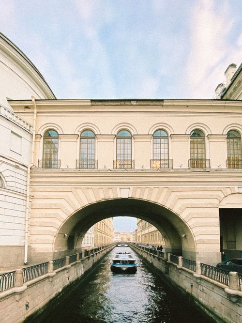 Free A serene view of a boat navigating through a historic city canal under an arch bridge. Stock Photo