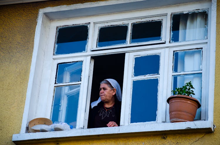 Old Woman Looking Out Of House Window