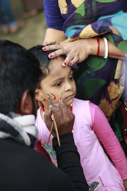 A Person Putting Face Paint on a Young Girl's Face