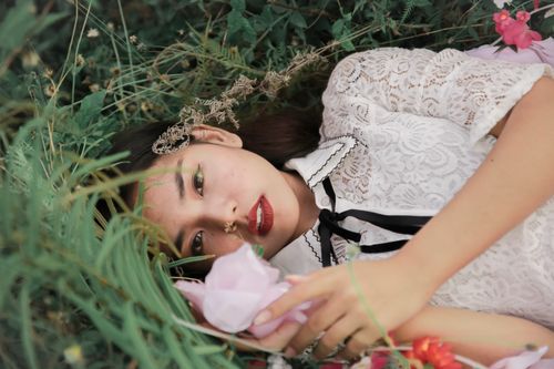 Free A woman in a lacy white dress lying among vibrant flowers outdoors. Stock Photo