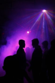 Silhouettes of people dancing under neon disco lights with a dramatic atmosphere.