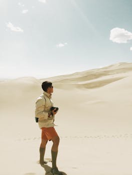 在晴朗的天空下，一位孤独的摄影师走过广阔的沙丘
