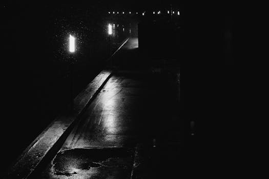 Dramatic black-and-white image of an empty street at night with glowing lights.