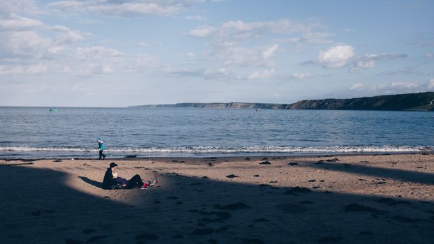 Serene beach scene with a lone figure relaxing on the sand under a clear blue sky.