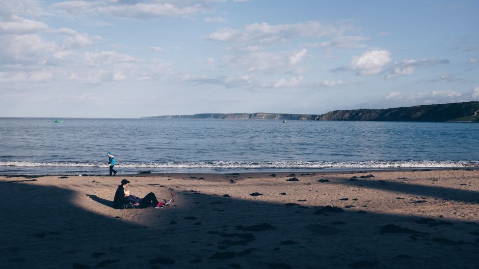 Serene beach scene with a lone figure relaxing on the sand under a clear blue sky.