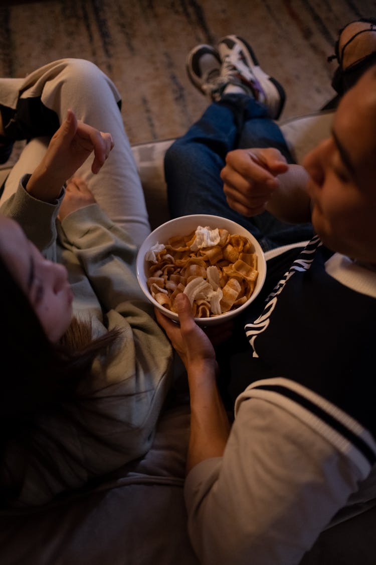 Man And Woman Sitting On The Couch And Eating Snacks