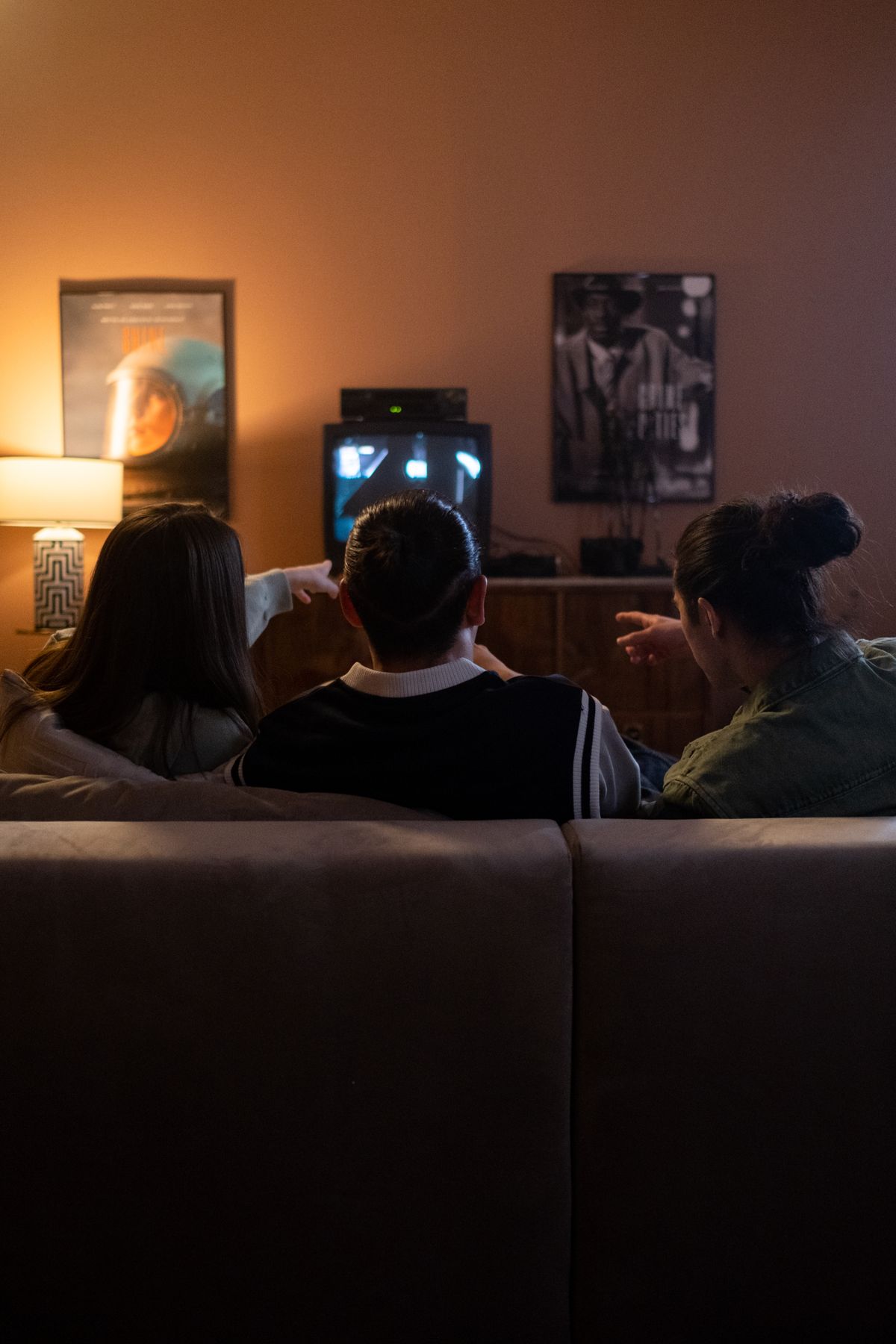 Three friends sitting on a couch watching TV together at night