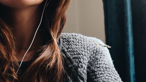 Free Close-up shot of a young woman wearing a gray knitted sweater with earphones in a cozy setting. Stock Photo