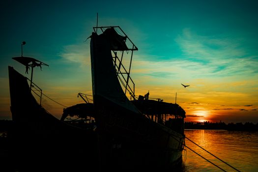 Silhouetted boats against a vibrant sunset over calm water, with a bird soaring in the sky.