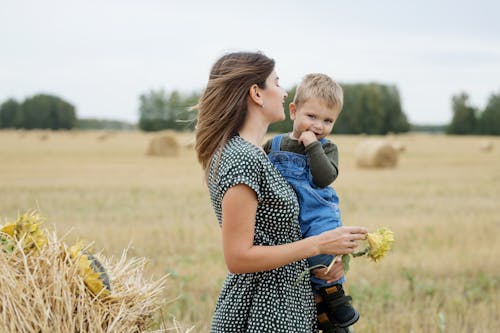 Woman Carrying Her Son while Holding a Yellow Flower