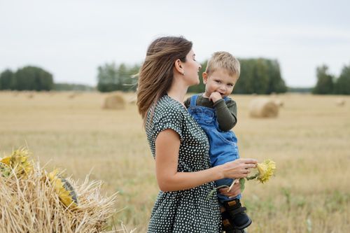 Free A heartwarming moment of a mother holding her son in a sunny hay field, capturing a bonding moment in nature. Stock Photo
