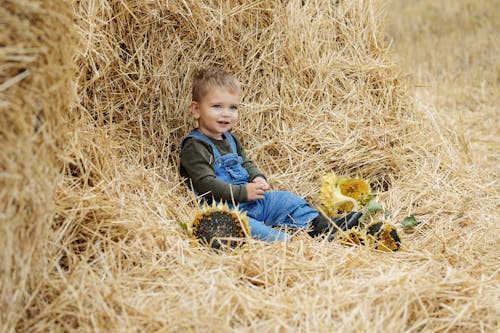 Photo of a Kid in a Denim Jumper Sitting on Hay